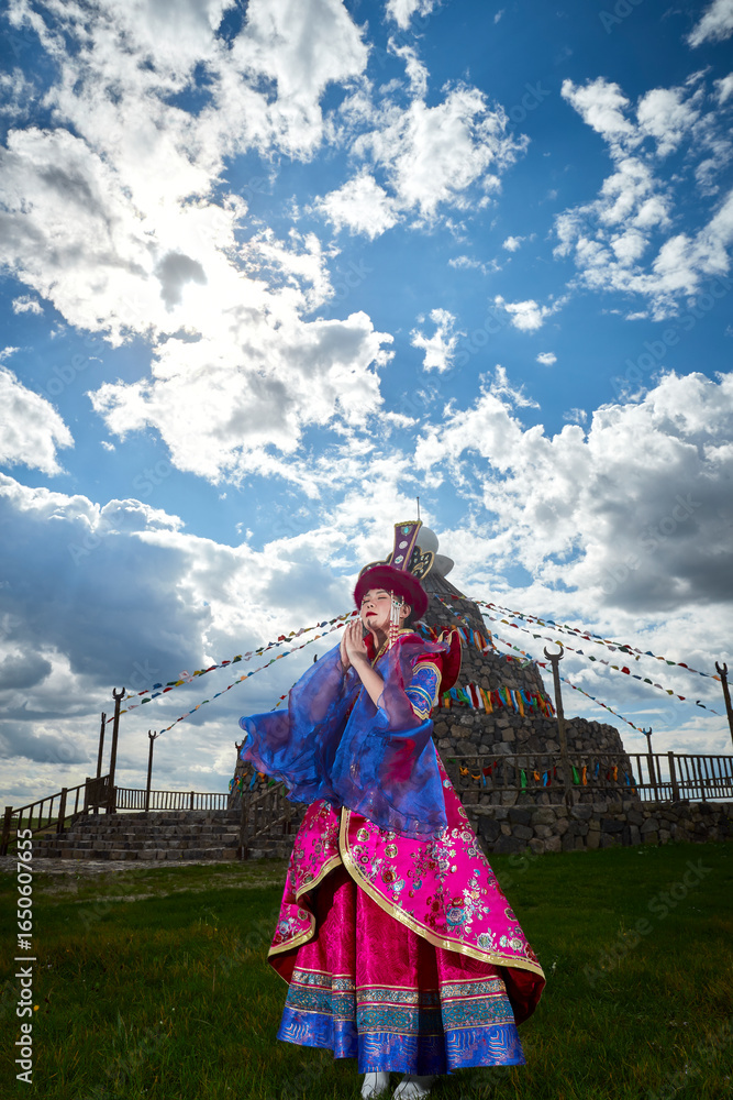 Fototapeta premium Mongolian girls dressed in luxurious Mongolian costumes in front of an obo on the grassland