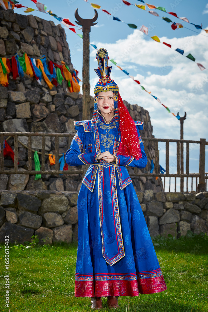 Naklejka premium Mongolian girls dressed in luxurious Mongolian costumes in front of an obo on the grassland