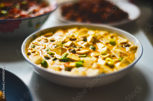 A bowl of creamy, yellowish soup with tofu and green vegetables, served alongside other dishes.