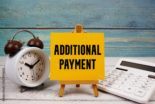 Additional Payment text written on paper card with calculator and alarm clock on wooden background