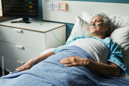 Photos Senior Caucasian woman lying in hospital bed with oxygen tube, resting with eyes