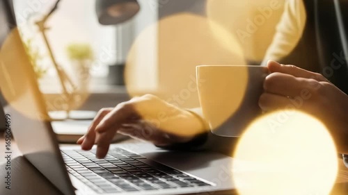 Person working on laptop and drinking coffee indoors