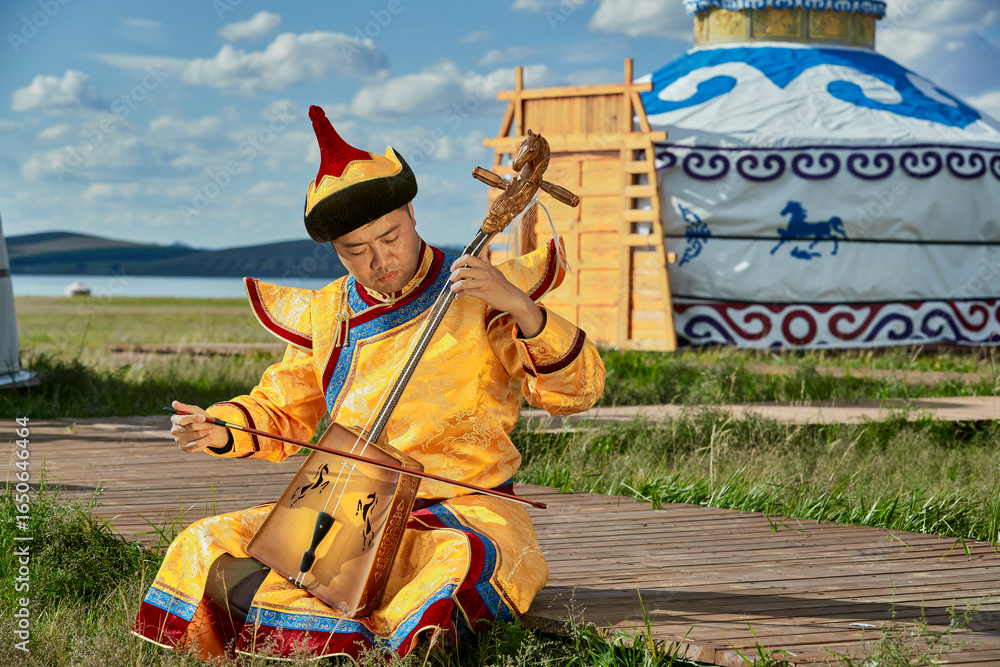 Ταπετσαρία A man dressed in Mongolian attire playing the morin khuur (horsehead fiddle) in front of a yurt