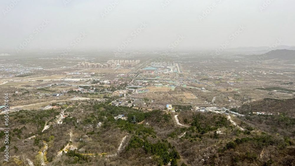 Obraz premium Aerial View of a Hilly Landscape with Urban Development in the Distance