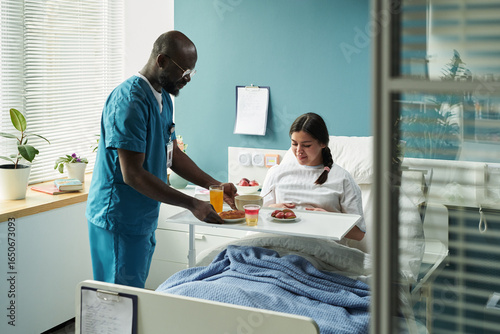 Photography Black male nurse serving breakfast to Caucasian pregnant woman patient sitting i
