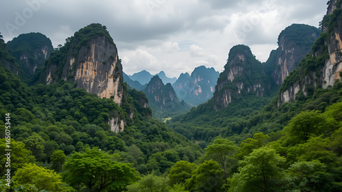 Dramatic limestone karsts rise majestically from a lush green forest under a cloudy sky in Thailand. This striking natural landscape showcases the rugged beauty of Southeast Asian mountains.