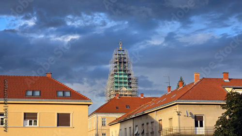 Foto Tall church tower covered in scaffolding dominates apartment rooftops with red t