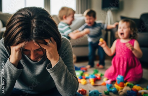 Exhausted parent sits on floor covering face, surrounded by mess and toys while toddlers cry in the background, showing emotional fatigue