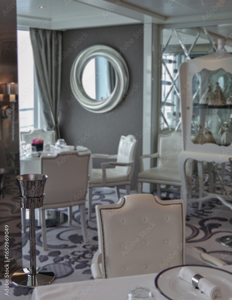 Fototapeta premium Formal and elegant a la carte ocean view dining room restaurant onboard luxury cruiseship or cruise ship liner with set tables in modern grey white silver Art Deco interior design style ambient light