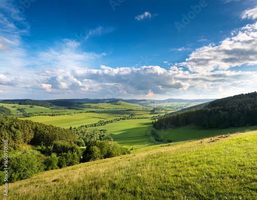 a serene landscape featuring a picturesque valley with fields forests and open land under a blue sky dotted with clouds