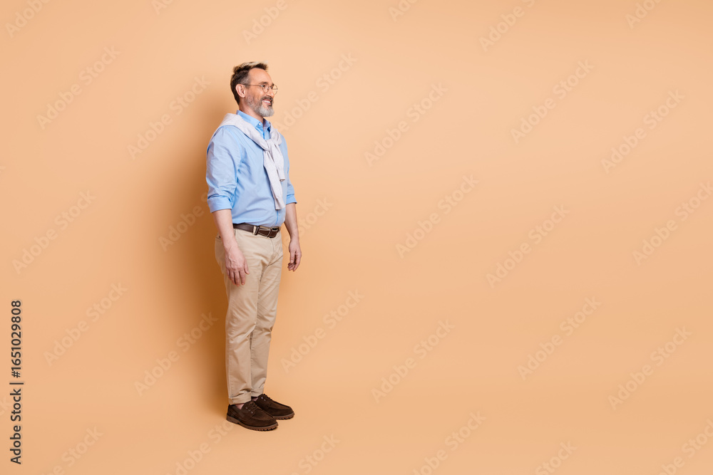 Fototapeta premium Confident mature businessman standing with casual elegance on beige background, showcasing stylish professionalism