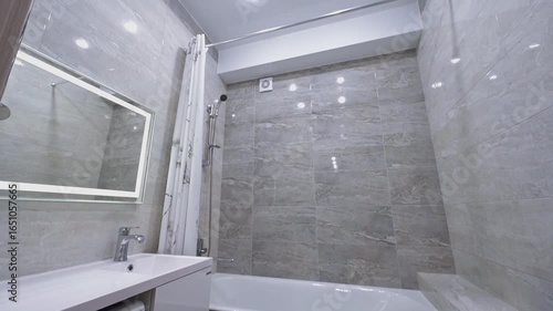 modern bathroom features gray marble-effect tiles, a white bathtub, and a vanity with an integrated sink and washing machine. A mirror hangs above the sink