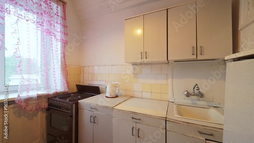 cozy kitchen with retro vibes, featuring a table with a floral tablecloth, a samovar, and vintage cabinets. The window is dressed with frilly pink curtains