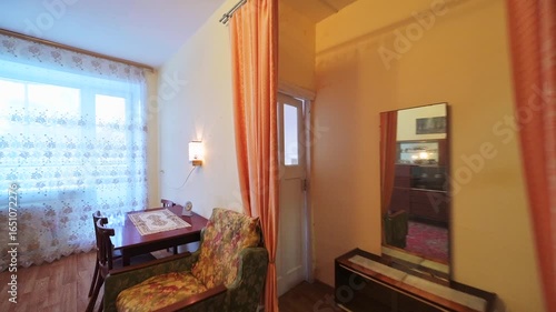 cozy living room with a small dining area. Features include a floral armchair, curtains, dark furniture, and a rug