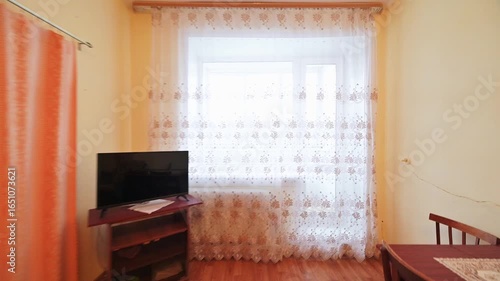 cozy living room with a small dining area. Features include a floral armchair, curtains, dark furniture, and a rug