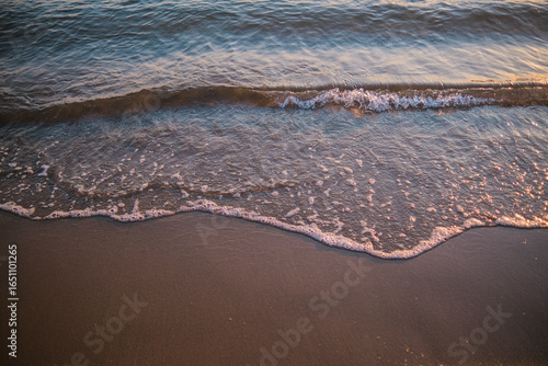 Fotografie Gentle ocean wave lapping sandy beach at sunset