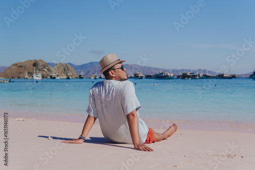 Back view of a young Asian man sitting and enjoying the pink beach scenery in Labuan Bajo.
