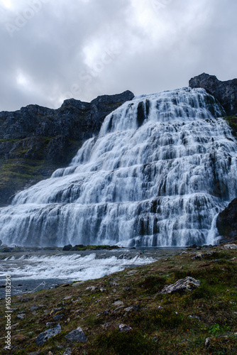Water flows dramatically from high cliffs into a serene river. Surrounded by lush greenery, this breathtaking waterfall captures the essence of Dynjandi waterfall Westfjords Iceland