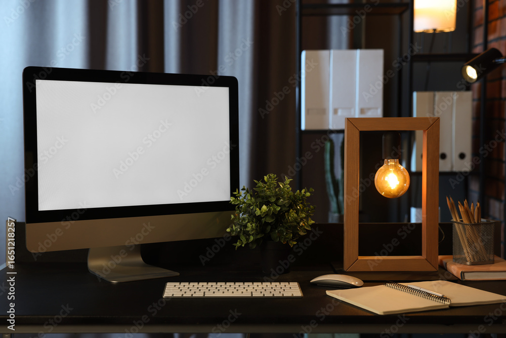 Fototapeta premium Computer, houseplant, lamp and stationery on black table indoors