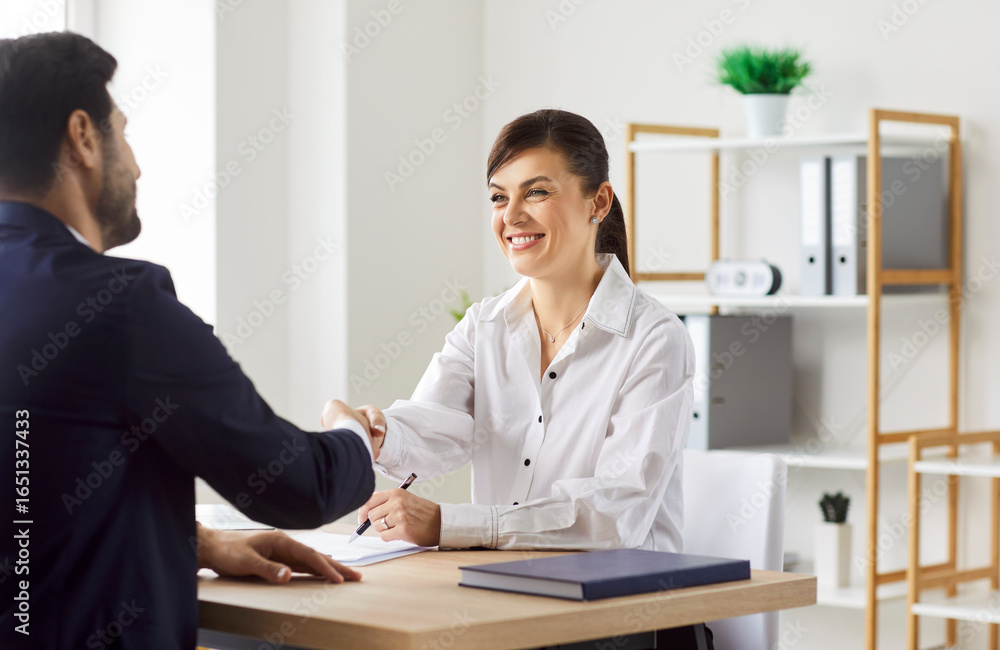 Obraz premium Businesswoman shaking client hand after successful deal, sitting at desk in office, satisfied hr manager hiring new male employee, business partners handshaking at meeting, corporate congratulation