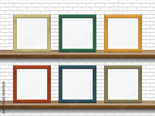 Six square frames are arranged in two rows on wooden shelves against a white brick background. Each frame is a different color. The frames are all empty and without pictures.