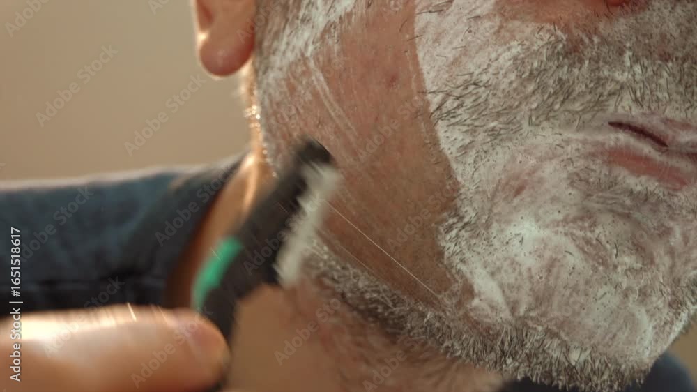 Close up of a man shaving his beard with a green and black razor Close up of a man shaving his beard with a green and black razor