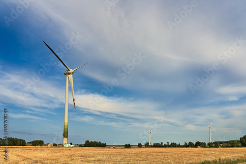 A wind turbine in a golden harvested field under a dramatic cloudy sky