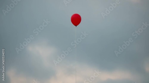 Lonely red balloon rises into overcast sky, symbol of hope and freedom