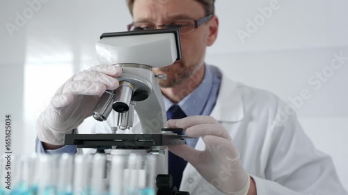 Man scientific researcher wearing white protective gloves carefully calibrating laboratory microscope, performing precision medical investigation. Medicine, healthcare and science concept