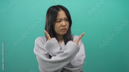 Woman pointing with hands in different directions against an isolated green background wall, expressing indecision or confusion.