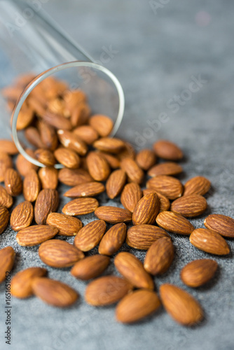 A glass jar spills fresh almonds on a gray stone surface, showcasing their natural texture.