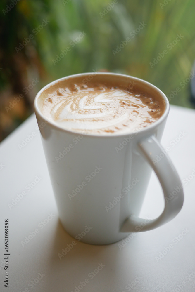 Obraz premium Coffee cup on a table with greenery behind