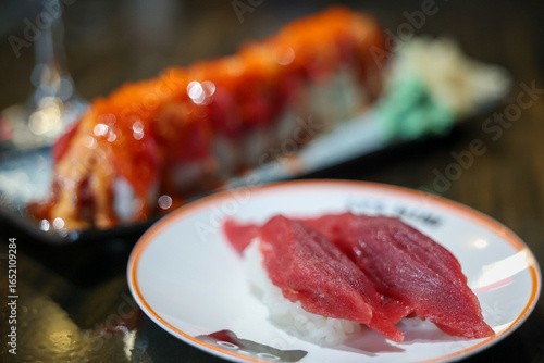 Fresh bluefin tuna nigiri on a plate at a sushi restaurant. Delicious raw fish over rice is healthy and tasty. In the background a fresh sushi roll topped with roe is on the table