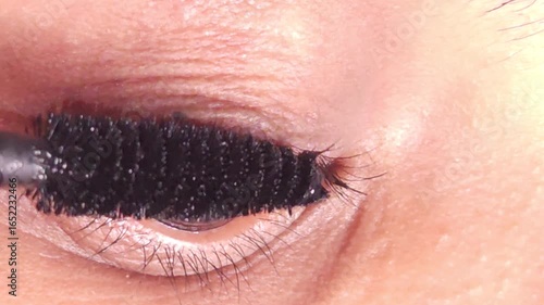 Young Indian girl with brown eyes applies black mascara on long eyelashes. Female paints artificial lashes with brush on blurred background macro, 4K resolution footage