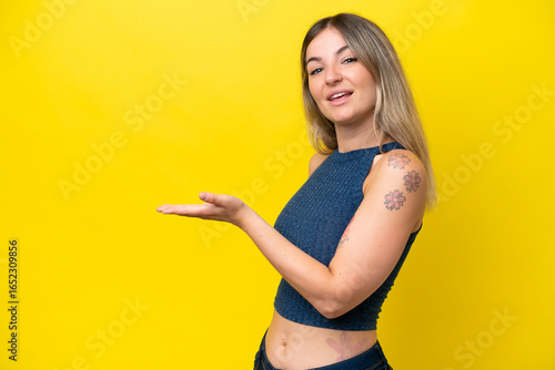 Young Rumanian woman isolated on yellow background presenting an idea while looking smiling towards