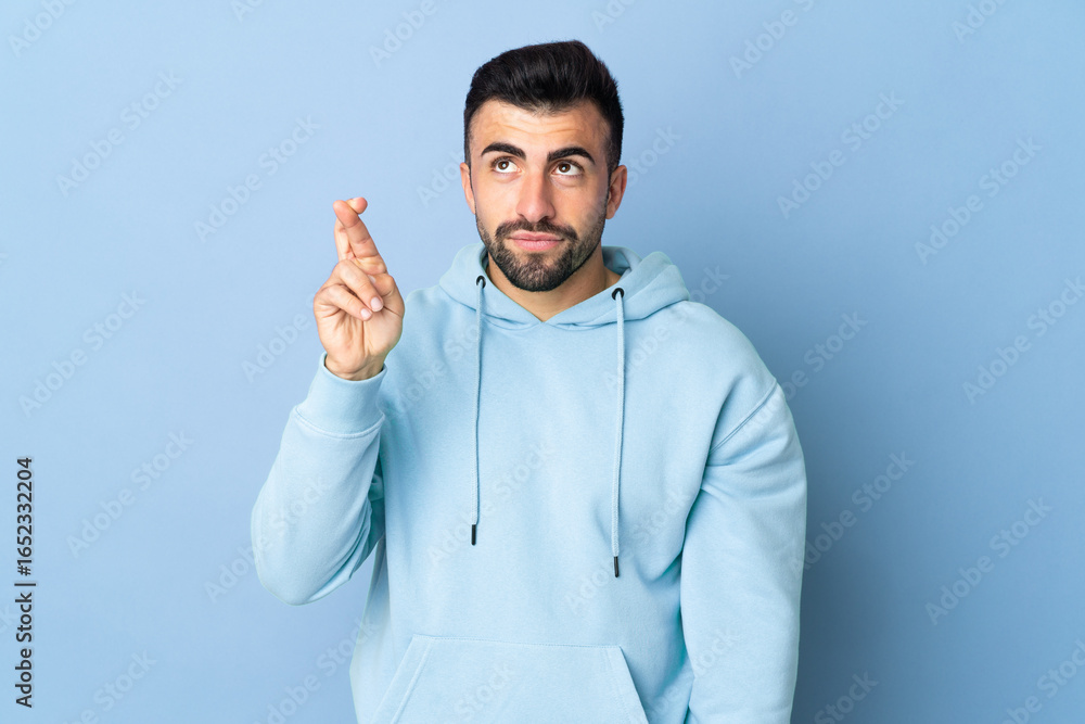 Fototapeta premium Caucasian man over isolated blue background with fingers crossing and wishing the best