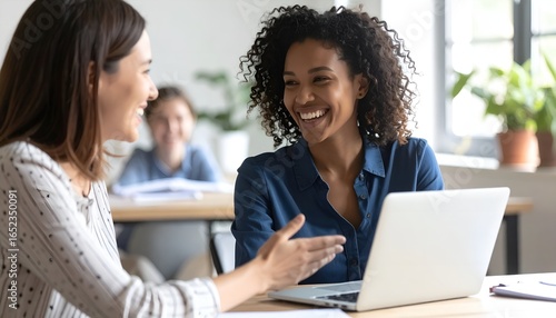 Close up happy young african american businesswoman using laptop with laughing female mentor in coworking boardroom at meeting. Smiling diverse woman managers. Detailed high quality image. 