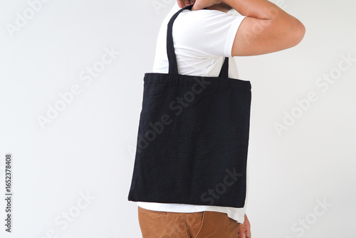 Young man hand holding black canvas tote bag on white background. Reusable eco bag for shopping. Eco friendly concept. Mockup for you designs.