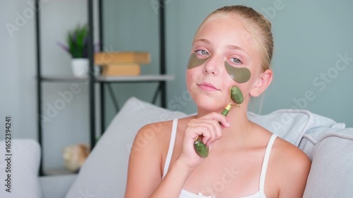 A girl is doing a facial massage with a massager. The teenager put gel patches under her eyes.