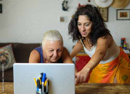 One woman teaches another to use the computer. The two women are thirty-eight and seventy years old respectively and are of Caucasian origin