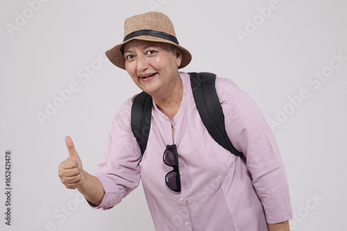 Indian happy senior woman wearing hat and sunglasses do thumbs up with both hands standing isolated on white studio background, Retirement life, summer holidays and travel.