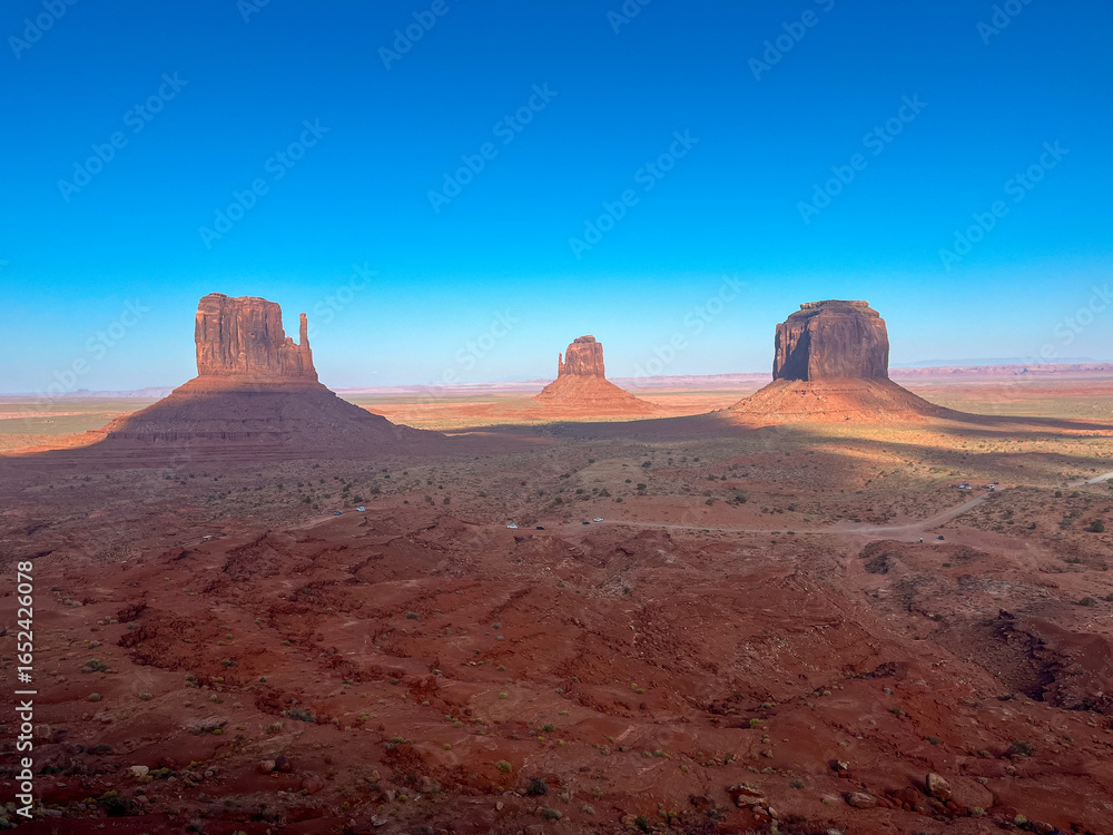 Fototapeta premium Monument Valley desert panorama with towering sandstone buttes under a bright blue sky.