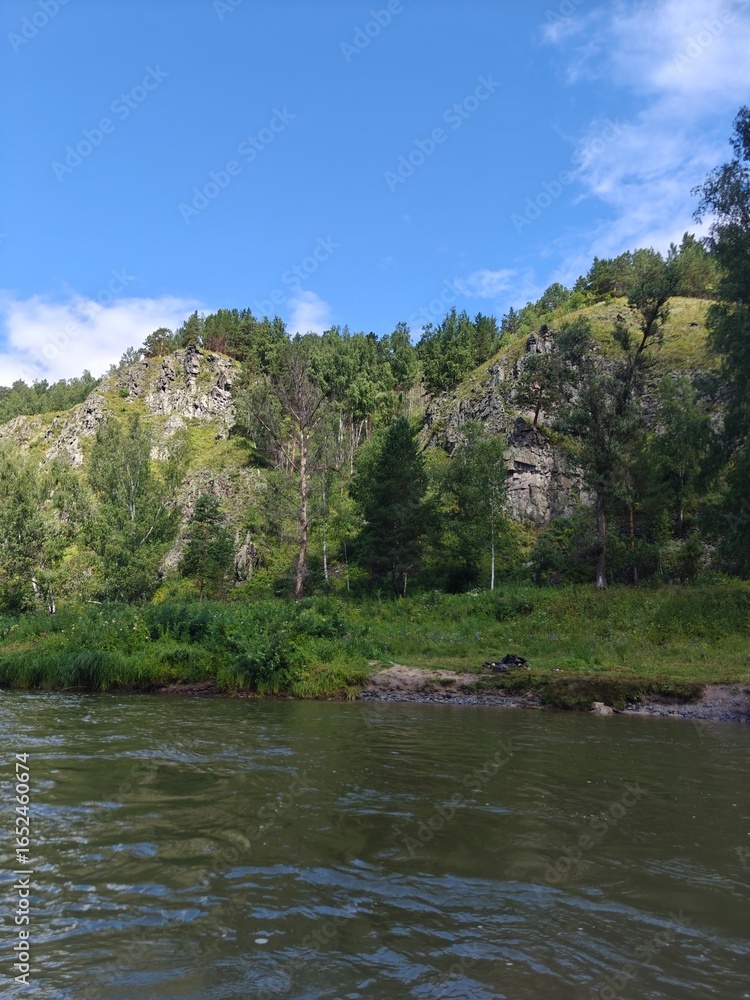 Fototapeta premium Serene River Landscape with Lush Greenery and Rocky Cliffs Under Blue Sky