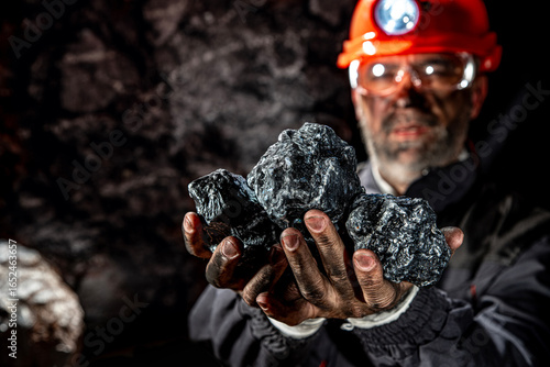 Fotografía Coal miner with a dirty face in black dust, wearing a protective helmet with a flashlight and work clothes for working in a mine
