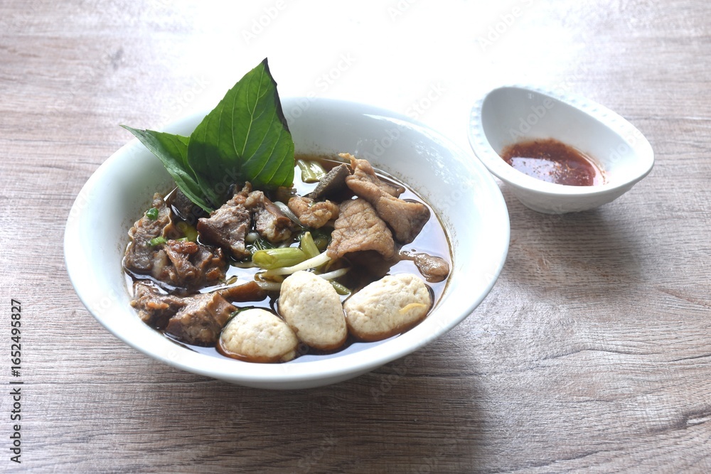 Fototapeta premium braised pork tendon and meatball with bean sprout toping fresh basil in brown soup on bowl dipping spicy sour chili sauce