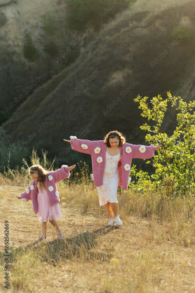 Fototapeta premium A young mother and daughter are walking in nature among the mountains in beautiful identical sweaters
