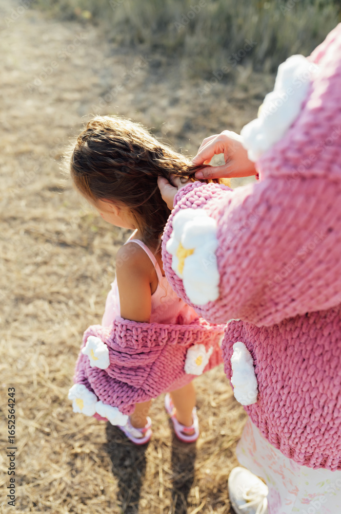 Obraz premium A young mother and daughter are walking in nature among the mountains in beautiful identical sweaters