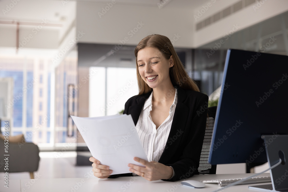 Positive young 20s legal expert, accountant woman reviewing papers, sales reports, text of agreement, sitting at workplace, reading financial business documents, smiling Positive young 20s legal expert, accountant woman reviewing papers, sales reports, text of agreement, sitting at workplace, reading financial business documents, smiling