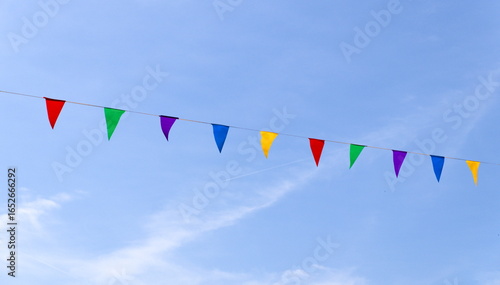 Time to party: festive decorations of colorful triangular bunting flags on a string strung across a blue sky with clouds