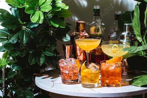 Set of alcoholic cocktails drinks with bottles on a marble table in a cozy environment of tropical plants